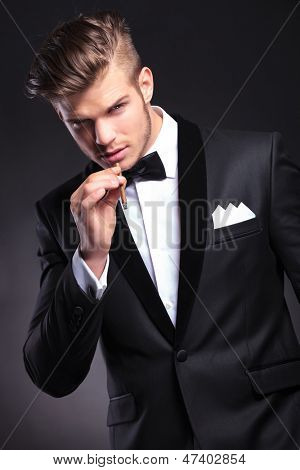 elegant unga mode man i smoking förbereder sig för att ta en rök från sin cigarett medan du tittar på th