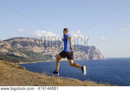 Lean Male Runner Run Mountain Trail Along Seashore, Sports Clothes Blue Shirt And Black Shorts, Summ