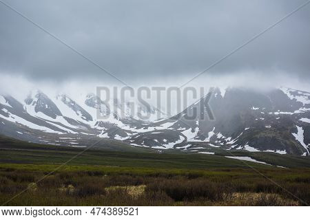 Dramatic Alpine Landscape With Snowy Mountains In Gray Low Clouds. Bleak Atmospheric Scenery Of Tund