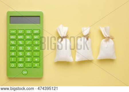 A Picture Of Calculator With 3 Money Bags. Payroll And Nfp Concept.