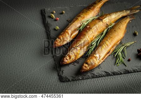 Smoked Capelin Fish On A Serving Board With Rosemary Served For Lunch. Dark Space For Menu Or Prescr