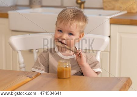 Happy Family At Home. Baby Boy Feeding Himself In Kitchen. Little Boy With Messy Funny Face Eats Hea