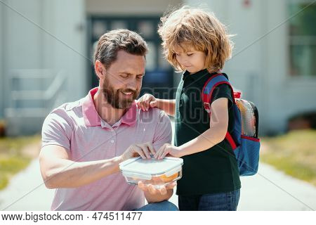 School Lunch For Kids. Father Supports And Motivates Son. Schoolboy And Parent In Shirt Holding Lunc