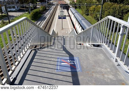 Train Station. No Smoking Sign In Front Of Station Stairs. View Of Track Platform With Passing Fast 