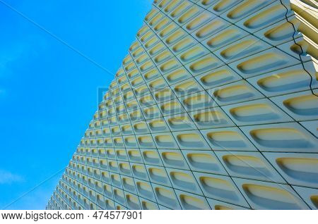 A bright blue sky is juxtaposed with a modern high rise building with a dramatically patterned facad