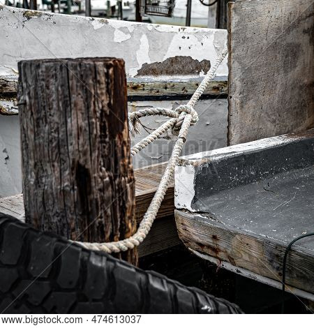 A Nautical Rope With A Single Knot, Tied Loosely To A Wooden Piling To Moor The Stern Of A Commercia