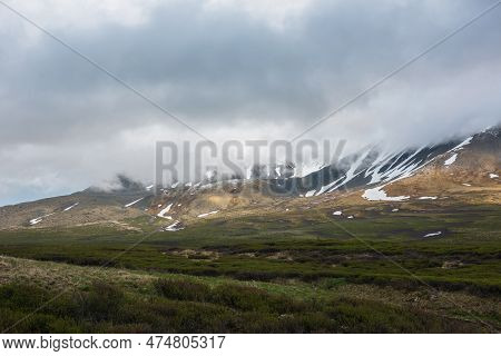 Dramatic Alpine Landscape With Snowy Mountains In Gray Low Clouds. Bleak Atmospheric Scenery Of Tund