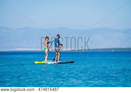 Couple Riding Sup Stand Up Paddle On Vacation.