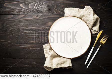 White Plate With Cutlary At Dark Wooden Table. Top View Image With Copy Space.