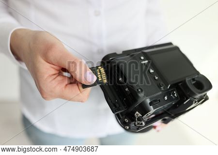 Female Camerawoman Puts Information Storage Device Into Camera Standing In Light Room. Young Woman P