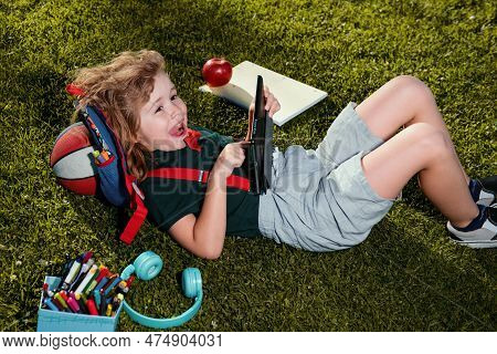 Kid With Tablet Device Sitting Outdoor In Garden, Wearing Short And Stripy Shirt. Lttle Child Outdoo