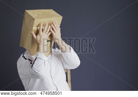 A Sad Man In A White Shirt With A Bag On His Head, With A Drawn Sad Emoticon Is Afraid, Closes His E