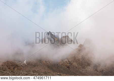 Scenic Alpine Landscape With Rocky Mountains In Dense Low Clouds In Morning Sunlight. Colorful Mount