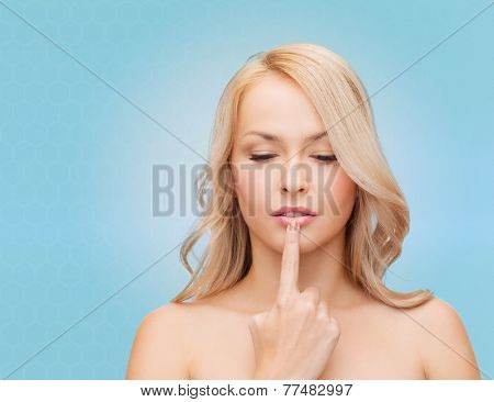 health, people and beauty concept - beautiful young woman touching her lips over blue background