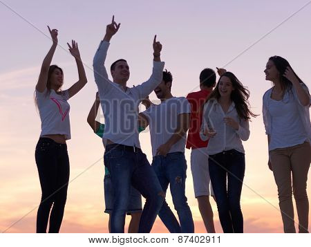 group of happy young people dancing and have fun on party in modern home bacony with sunset and ocean in background