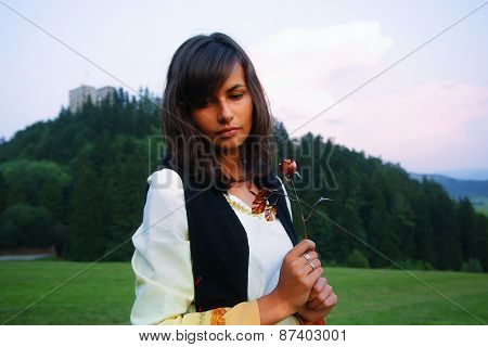 A beautiful girl in historical costume in a wild meadow landscape holding a secretful romantic rose