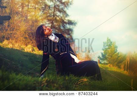 A beautiful young woman with dark hair and a historical dress posing on a meadow in open lanscape