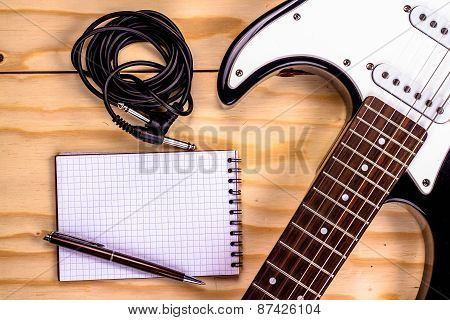 electric guitar and memo pad on wooden table.