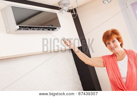 Woman holding a remote control air conditioner at home. Happy mature woman on sofa
