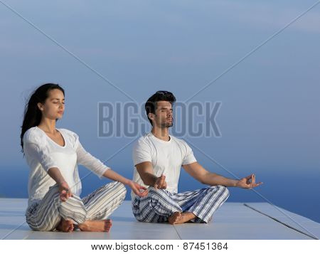 young couple practicing yoga at sunset in modern home terace with ocean and sunset in background