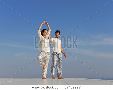 young couple practicing yoga at sunset in modern home terace with ocean and sunset in background