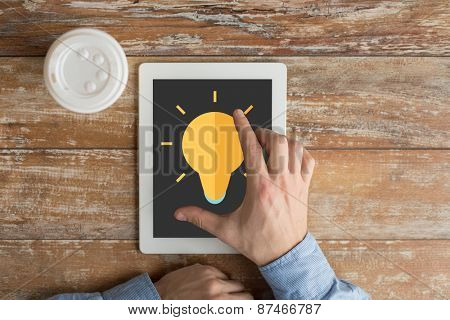 business, education, inspiration, people and technology concept - close up of male hands with lighting bulb icon on tablet pc computer screen and coffee cup at table