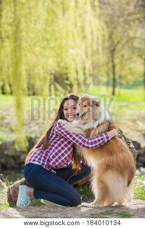 Young beautiful woman with long hair in an embrace with a collie dog. Outdoors in the park.