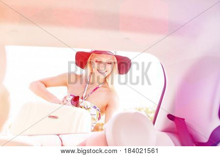 Happy woman loading suitcase in car trunk