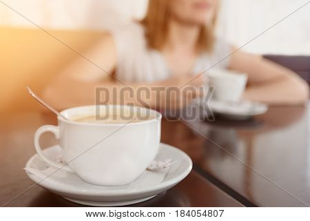 Selective focus on a cup with aromatic coffee. Blurred background with girl drinking coffee cup.