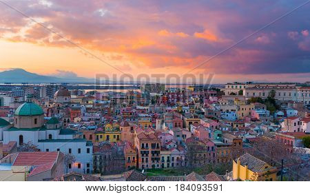 Sunset on Cagliari, panorama of the old city center with traditional colored houses, mountains and beautiful yellow-pink clouds in the sky, Sardinia Island, Italy
