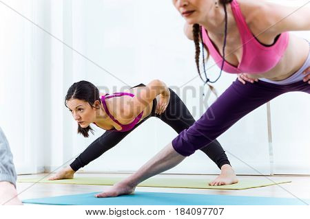 Portrait of two beautiful young women practicing yoga at home. Prasarita Padottanasana pose.