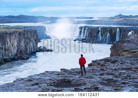 Selfoss waterfall. Guy in a red jacket looks at a cascade of water. Famous tourist attraction of Iceland. Beauty in nature