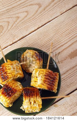 Corn cobs cooked on a grill on a wooden background. Corncobs on wooden skewers