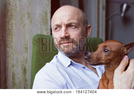 Dog And Its Owner Look Thoughtfully Out The Window, Watching The Street. Friendship Between A Dog An