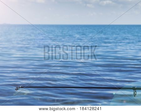 The tip of a fishing rod with a line outgoing into the sea
