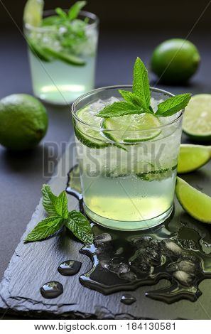 Cold cocktail with lemon liqueur, lime, tonic, ice in two glasses or mojito cocktail on dark background, copy space. Vertical. Close-up.