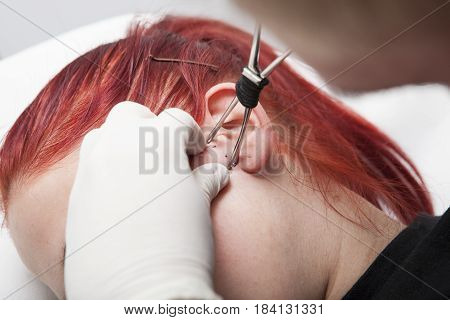 Piercing professional gripping the skin ear before inserting the cannula. Tragus type