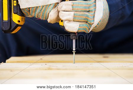 Close up of pair of hands in work gloves drilling a screw into wood with an electric drill