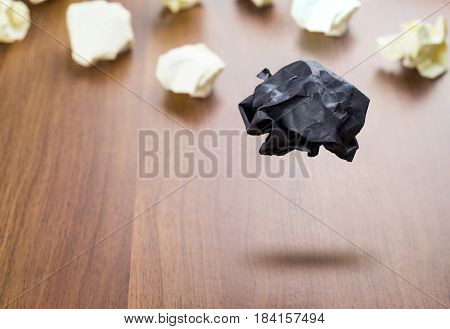Black Crumpled Paper Ball Floating Around White Paper Ball On Wood Table, Business Concept