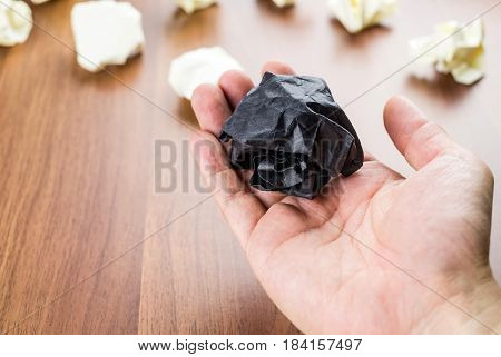 Black Crumpled Paper Ball On Open Hand At Wood Table Top, Business Concept