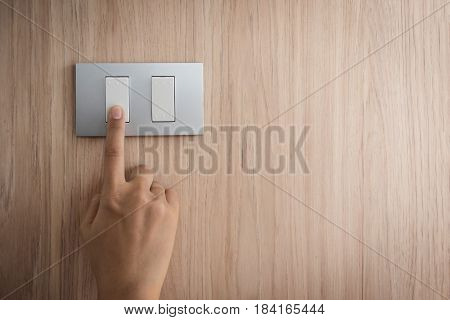 Close up hand turning on or off on grey light switch with wooden background. Copy space.