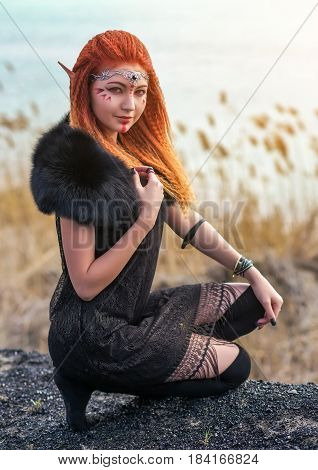 Elf women with fiery hair on nature. Beautiful young fantasy girl. Cosplay character