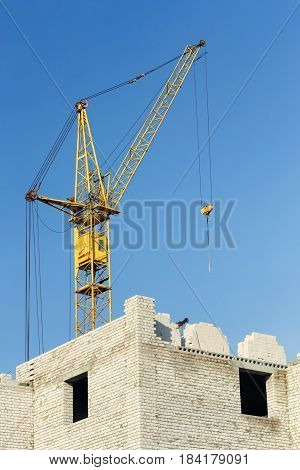 Small construction project of multistorey housing building. Residential building construction site with unfinished building and yellow crane against blue sky