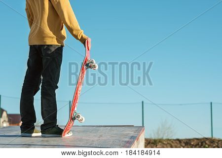 close-up A teenager standing in a yellow hoodie holds a hand skateboard against the backdrop of the outskirts of the city's shantytown and blue sky.