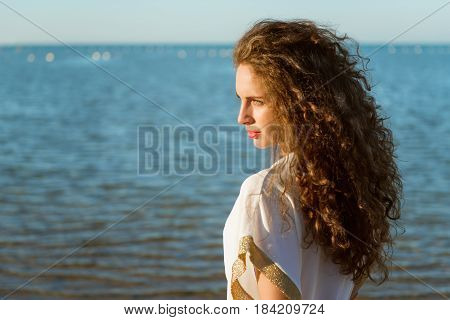 Young beautiful lady with long curly hair looking far on the beach
