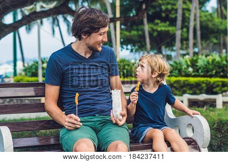 Father And Son Eat Fried Sweet Potatoes In The Park. Junk Food Concept