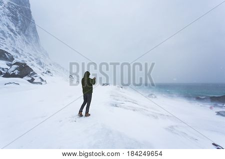 The man takes a picture using the phone of the winter landscape of Lofoten during the blizzard