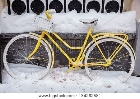 Motionless yellow bicycle with white wheels and basket in the snow