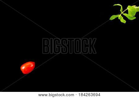 Top view of single cherry tomato on one side and mint leaves diagonally opposite isolated on a black background. Minimalist picture style with copy space for text