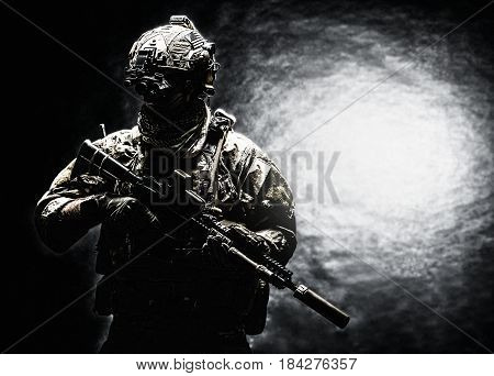 Army soldier in Combat Uniforms with assault rifle, plate carrier and combat helmet are on, Shemagh Kufiya scarf on his neck. Studio shot, dark background